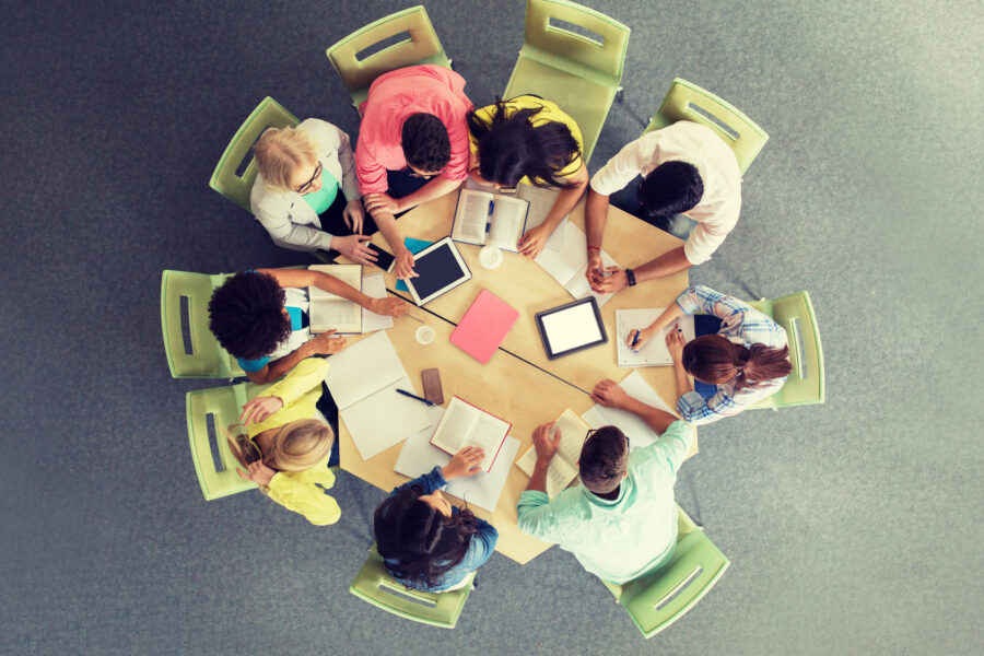Bildet viser en gruppe mennesker som sitter rundt et bord å jobber med bøker og nettbrett.