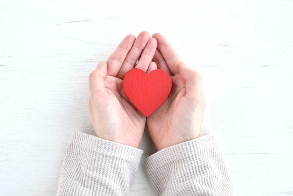Bilde som viser to hender som holder et rødt hjerte laget av treverk